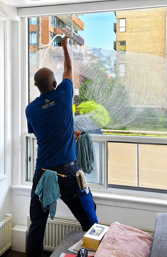 Bright Shine cleaner carefully cleaning a large interior residential window
